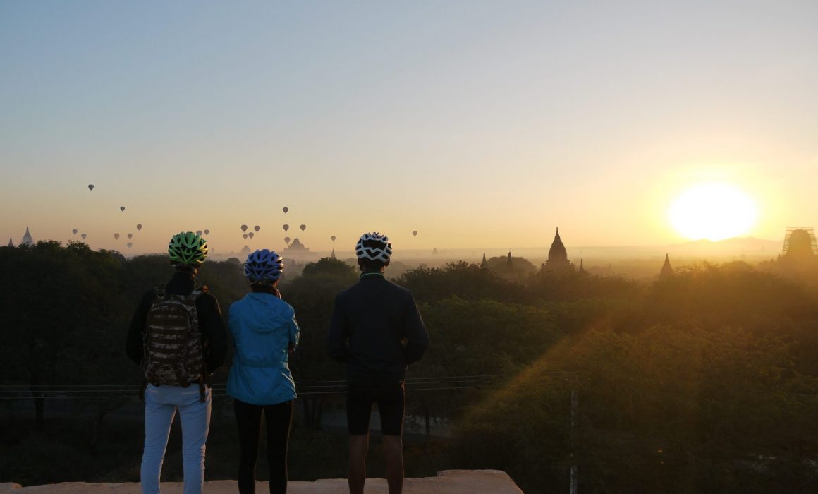 three cyclists in helmets watching balloons over Bagan at sunrise