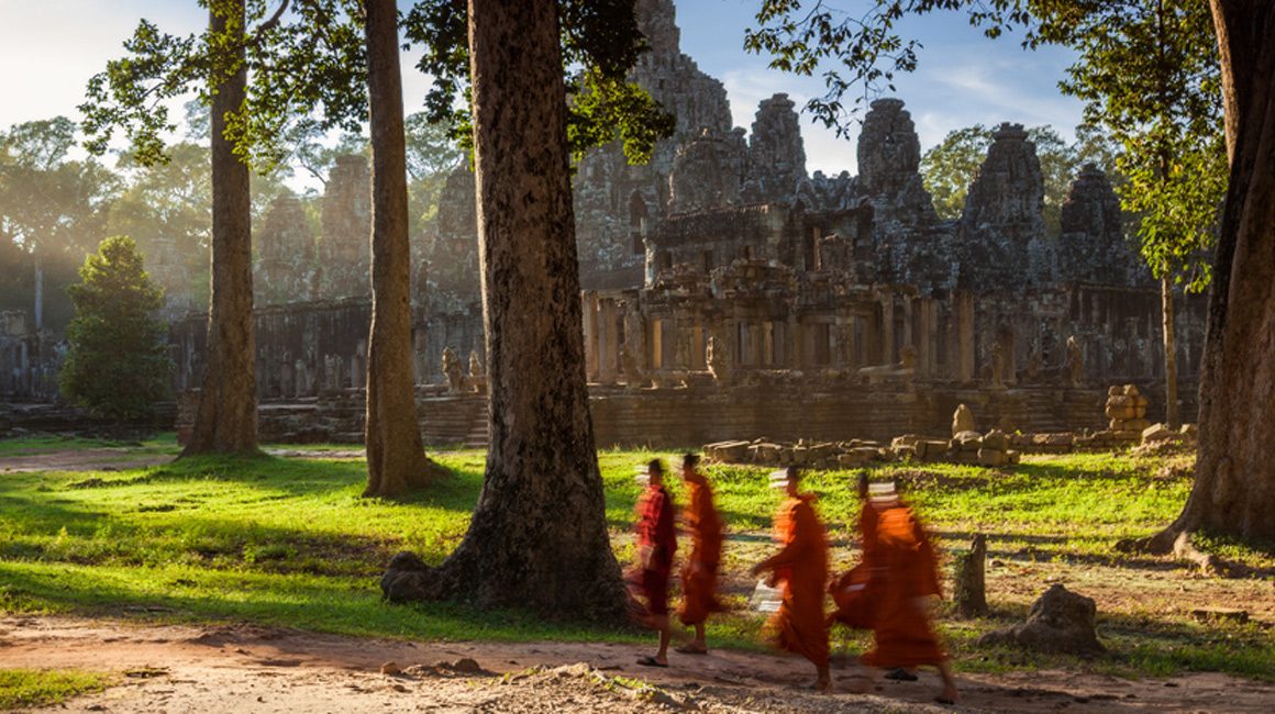 Five monks in orange robes walking in front of Bayon temple