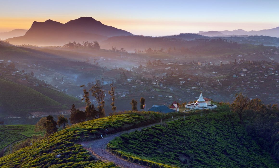 Curved path to white stupa with mountains and sunset behind