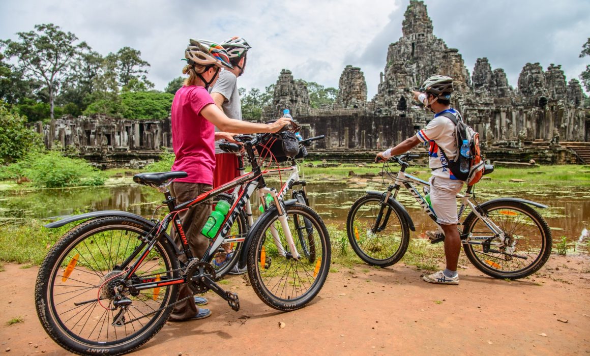 Guide pointing to Bayon temple and talking to two cyclists