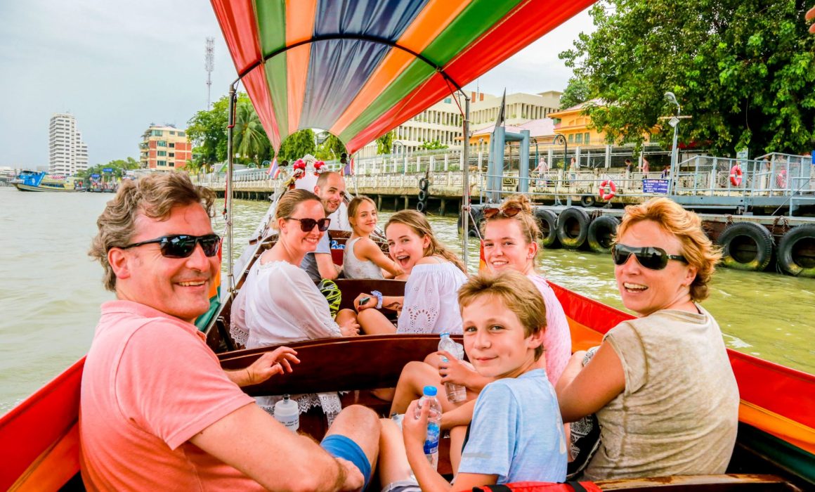 Group of eight tourists, some children, looking back and smiling on boat in the canals of Bangkok