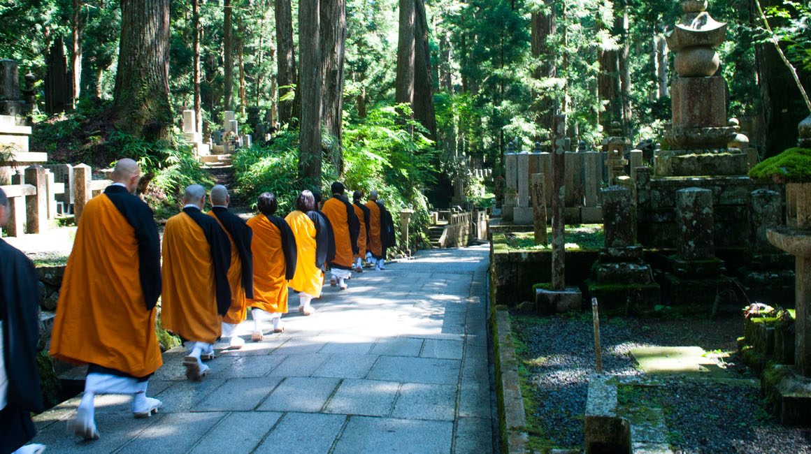 Monks in orange robes walking through cemetery in forest