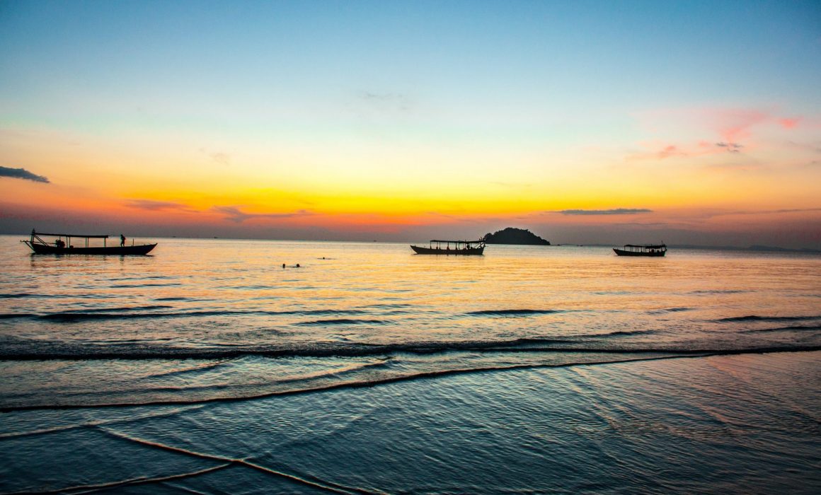 Water breaking on shore with sunset and boats on horizon