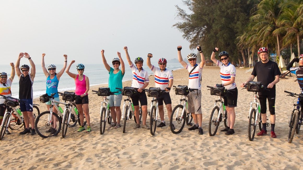 Group of eleven cyclists raising arms in the air on the beach in Phuket, Thailand