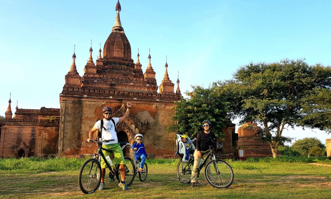 Family with two young children on bikes in front of temple in Myanmar