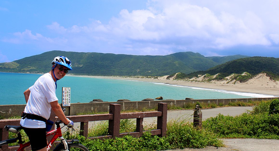 Smiling cyclist turning around with coastline of Taiwan behind