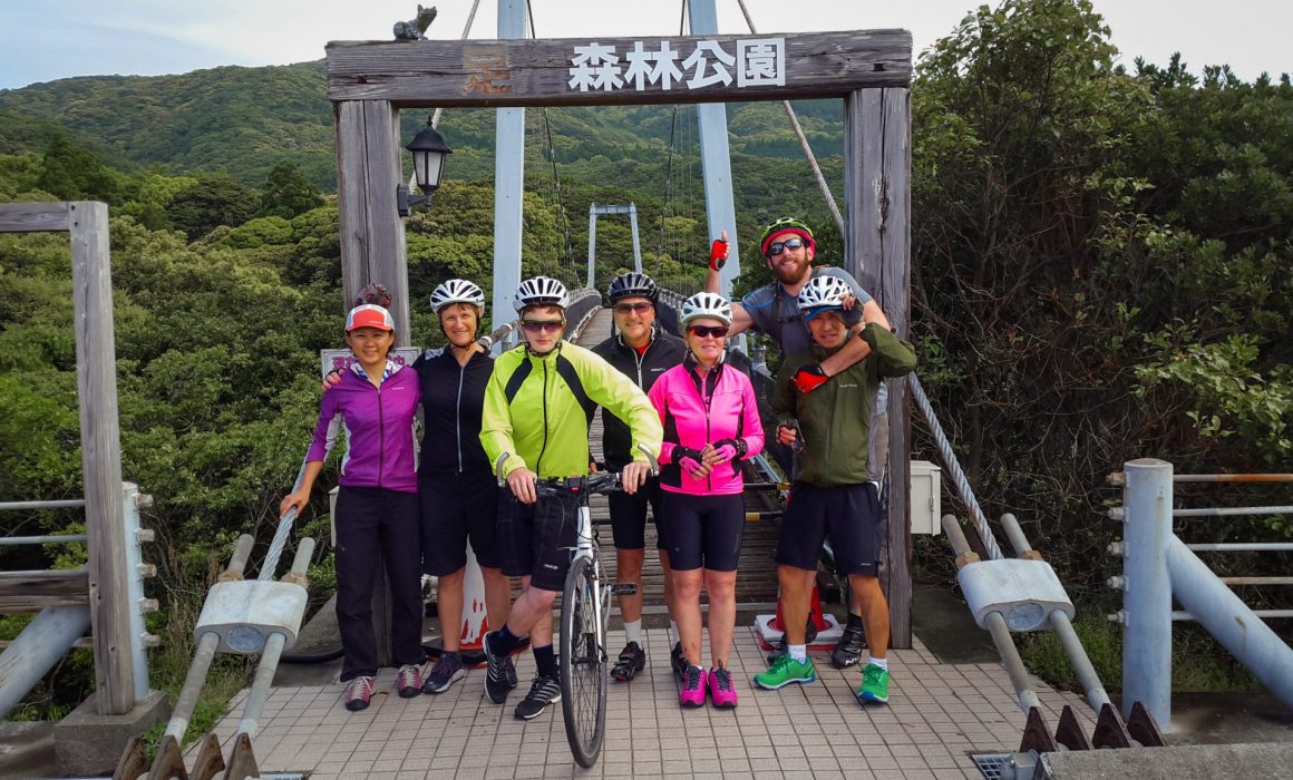 Group of cyclists in helmets in front of suspension bridge in Japan