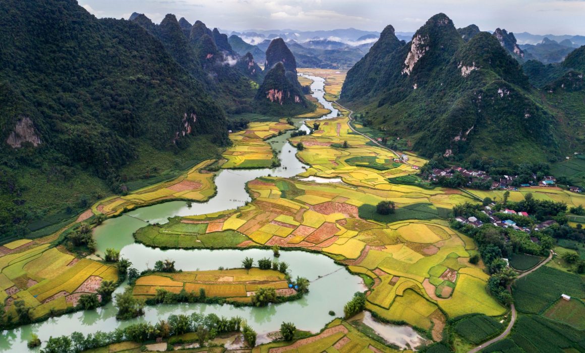 Patchwork fields around winding river with tall mountains covered in green in Vietnam