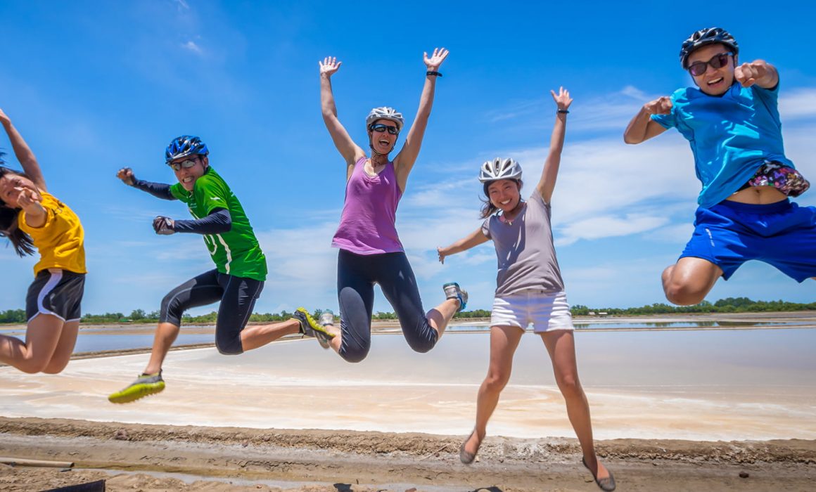 Five cyclists in helmets jumping in the air above sand