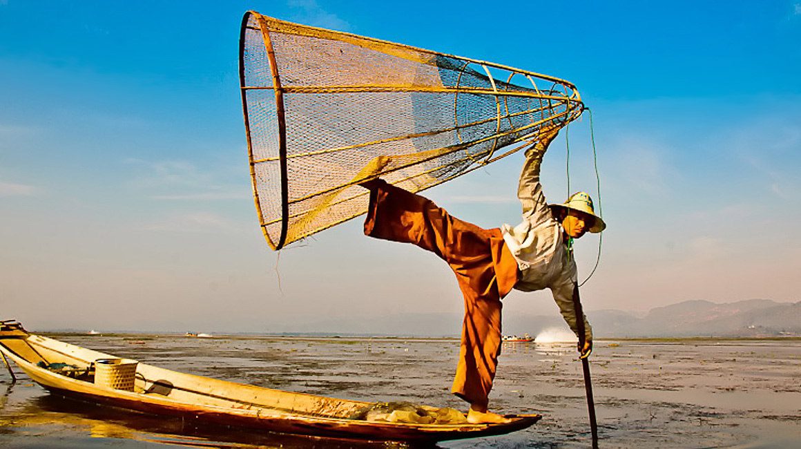 One leg fisherman holding net and rowing on Inle Lake