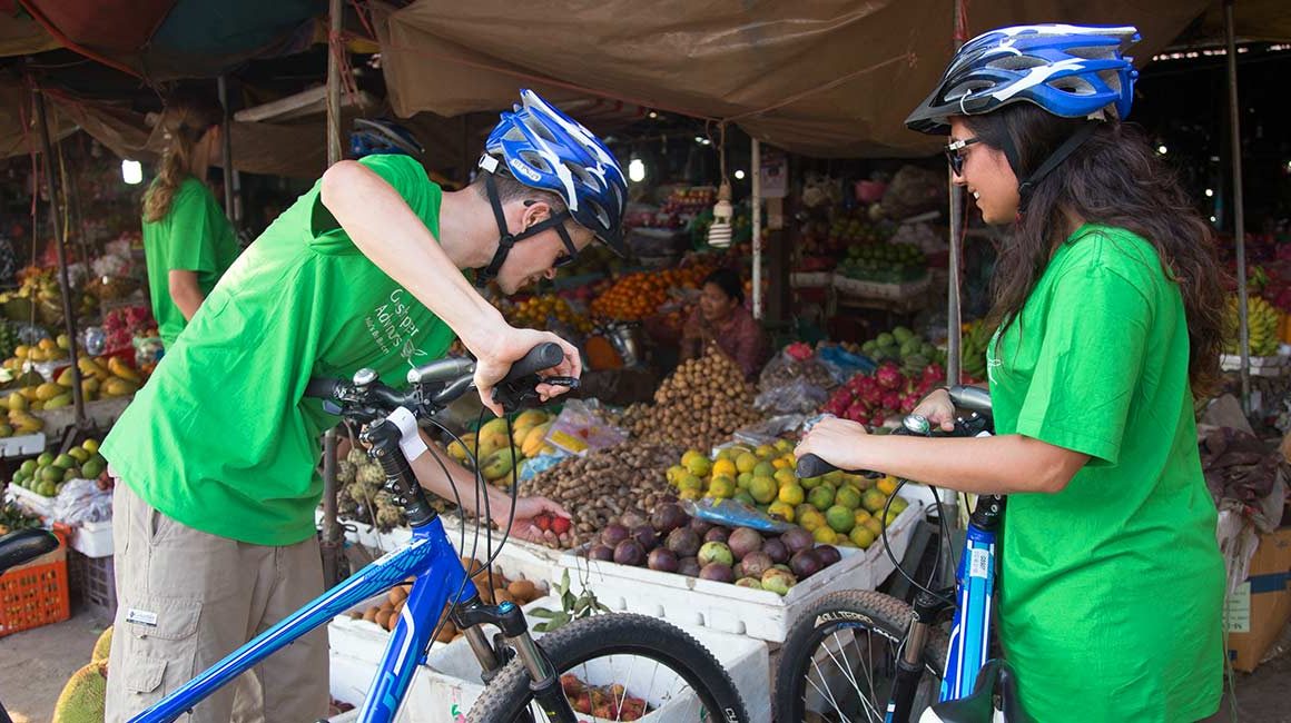 Two cyclists in helmets inspecting fruit at local market in Phnom Penh