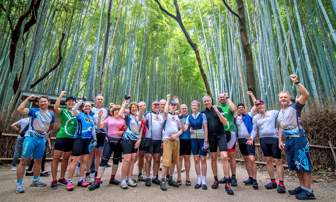 Group of cyclists raising arms in forest in Japan