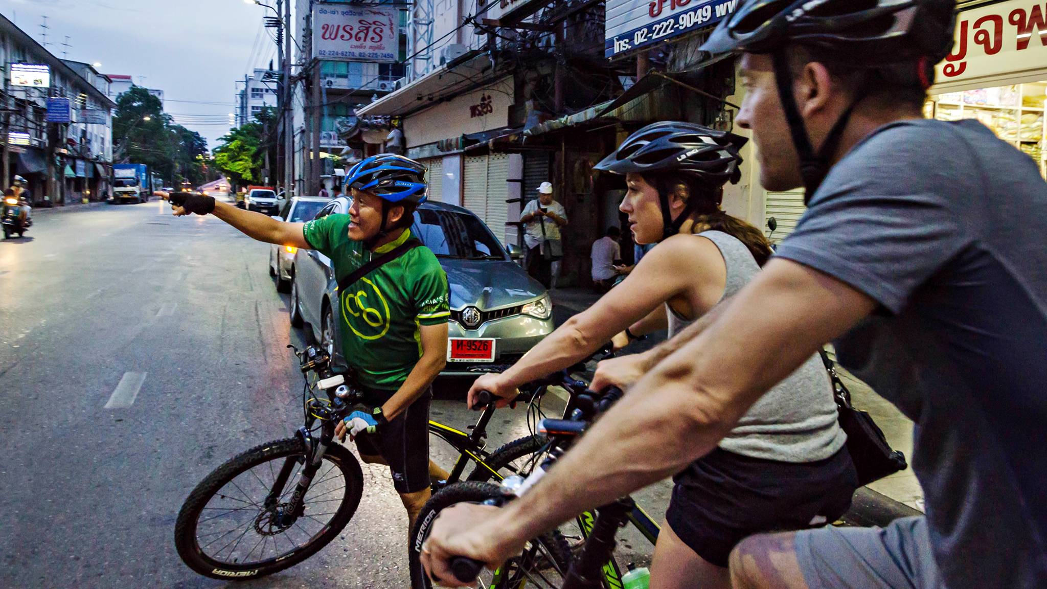 Guide pointing at something across the street and two tourists on bicycles in Bangkok