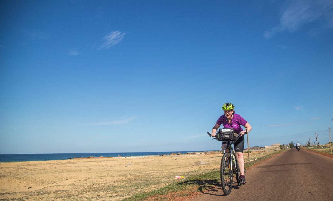 Cyclist riding road past sand and water